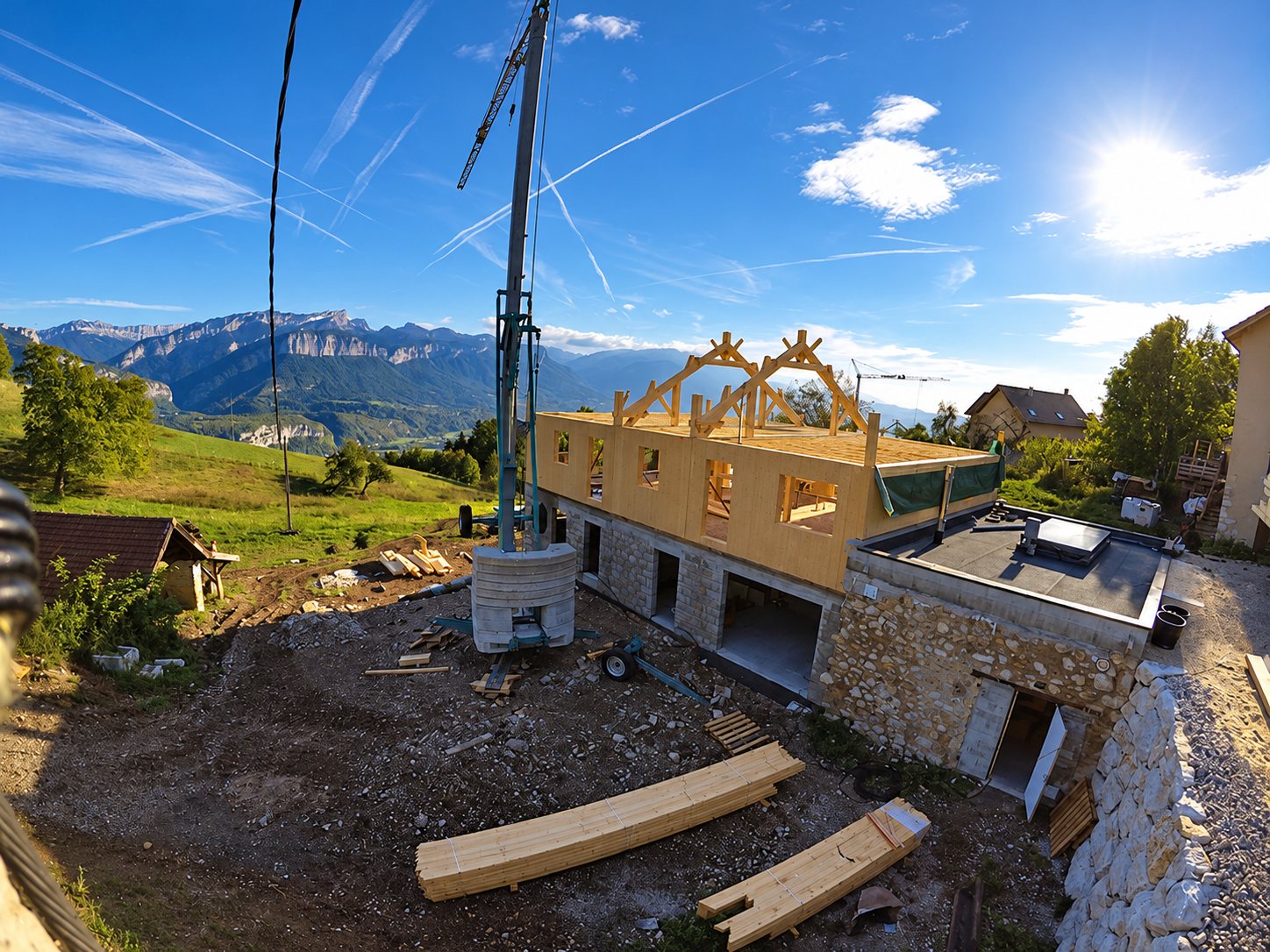 Chantier d'une maison en cours de construction avec ossature et charpente en bois sur un rez-de-chaussée en pierre, une grue et des montagnes en arrière-plan.