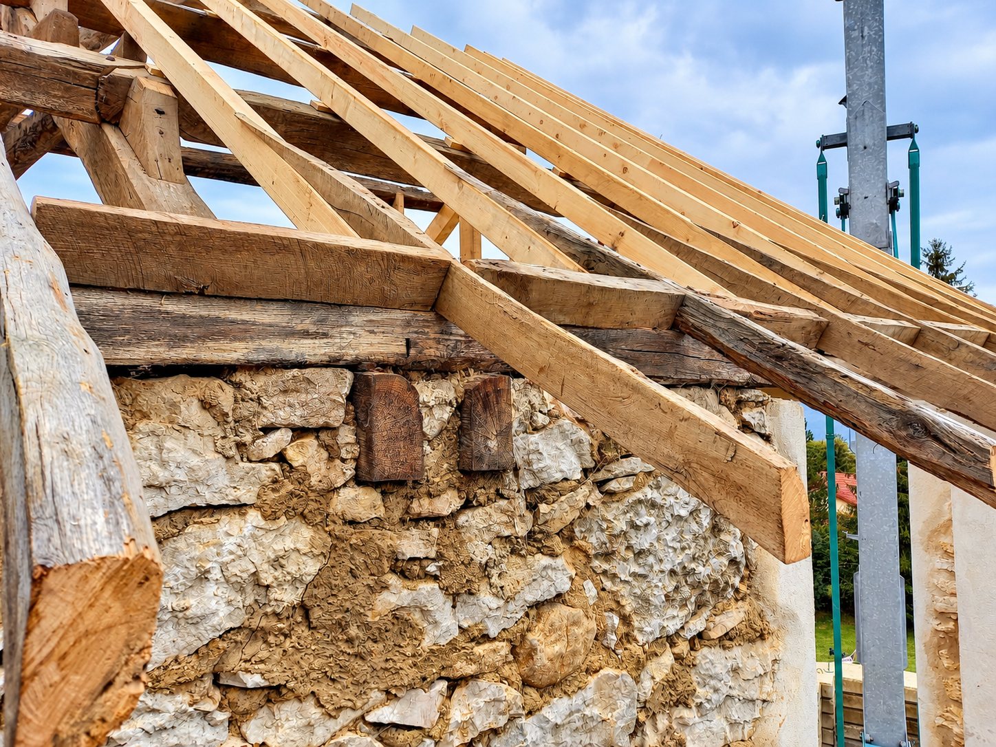 Gros plan sur une charpente en bois posée sur un ancien mur en pierres liées à la terre, sur un chantier de rénovation.